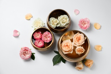 Photo of Tibetan singing bowls with water and different beautiful rose flowers on white background, flat lay