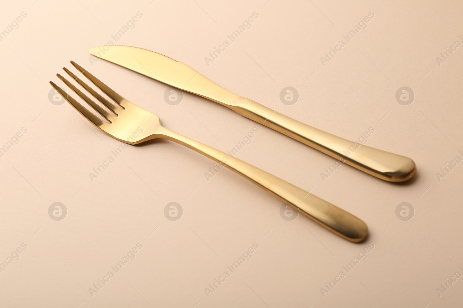 Photo of Stylish cutlery. Golden knife and fork on beige table