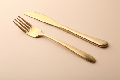 Stylish cutlery. Golden knife and fork on beige table