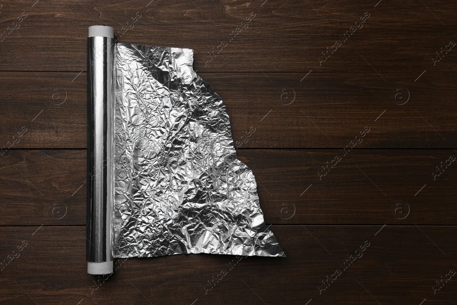 Photo of Roll of foil paper on wooden table, top view. Space for text