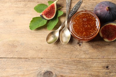 Photo of Glass jar with tasty sweet jam, spoons and fresh figs on wooden table, flat lay. Space for text