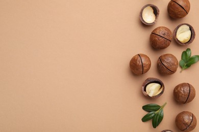 Photo of Tasty Macadamia nuts and green leaves on beige background, flat lay. Space for text