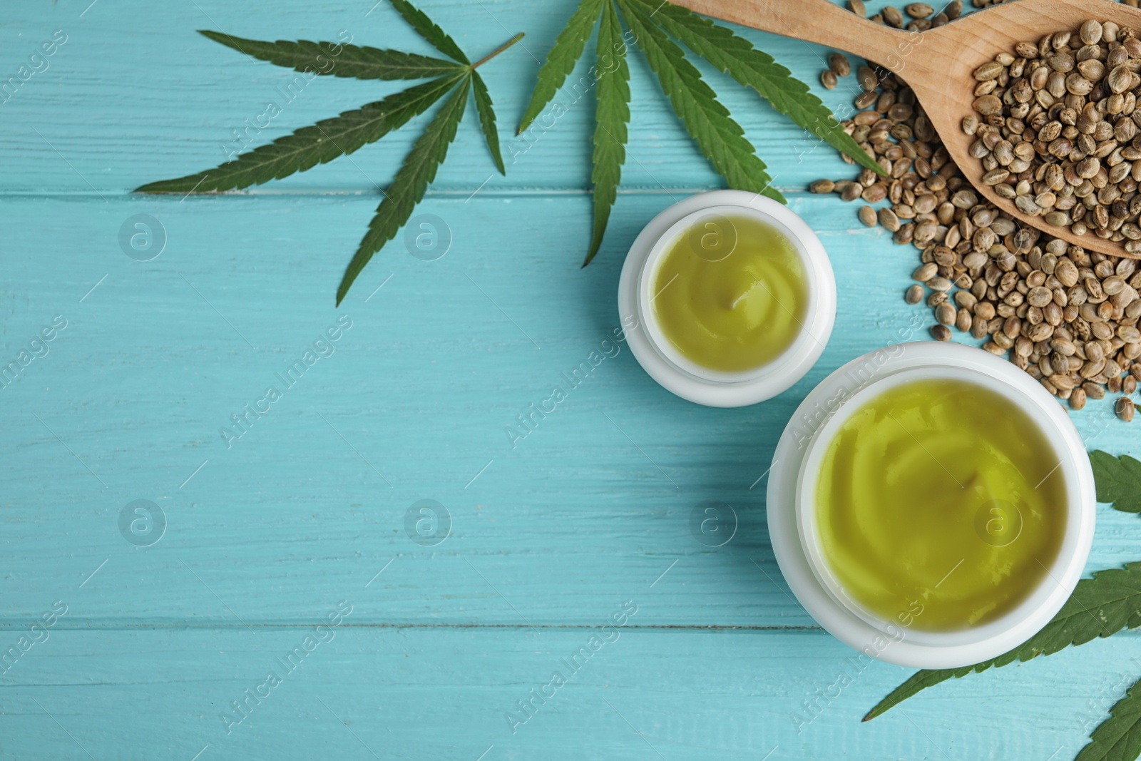 Photo of Jars of hemp cream and seeds on blue wooden table, flat lay with space for text. Organic cosmetics