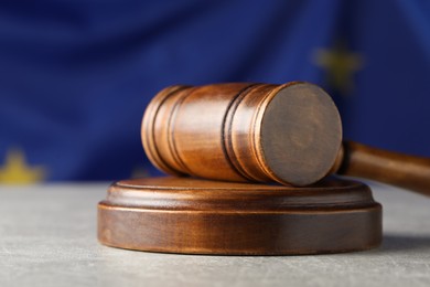 Wooden judge's gavel on grey table against European Union flag, closeup