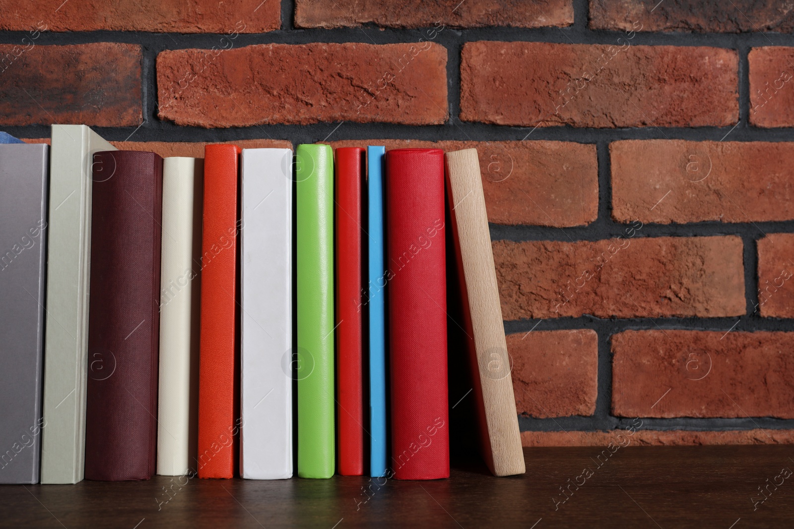 Photo of Many hardcover books on wooden table near brick wall