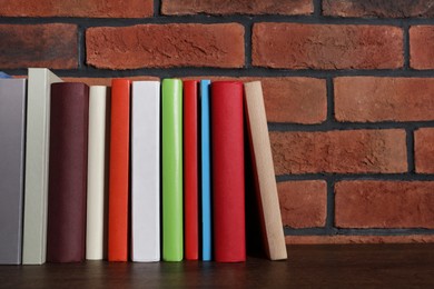Many hardcover books on wooden table near brick wall