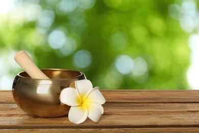 Image of Golden singing bowl, mallet and flower on wooden table outdoors, space for text