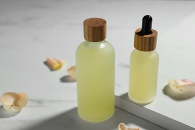 Bottles of essential oil and flower petals on white marble table