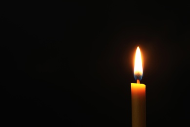 Burning candle on dark background, space for text. Symbol of sorrow
