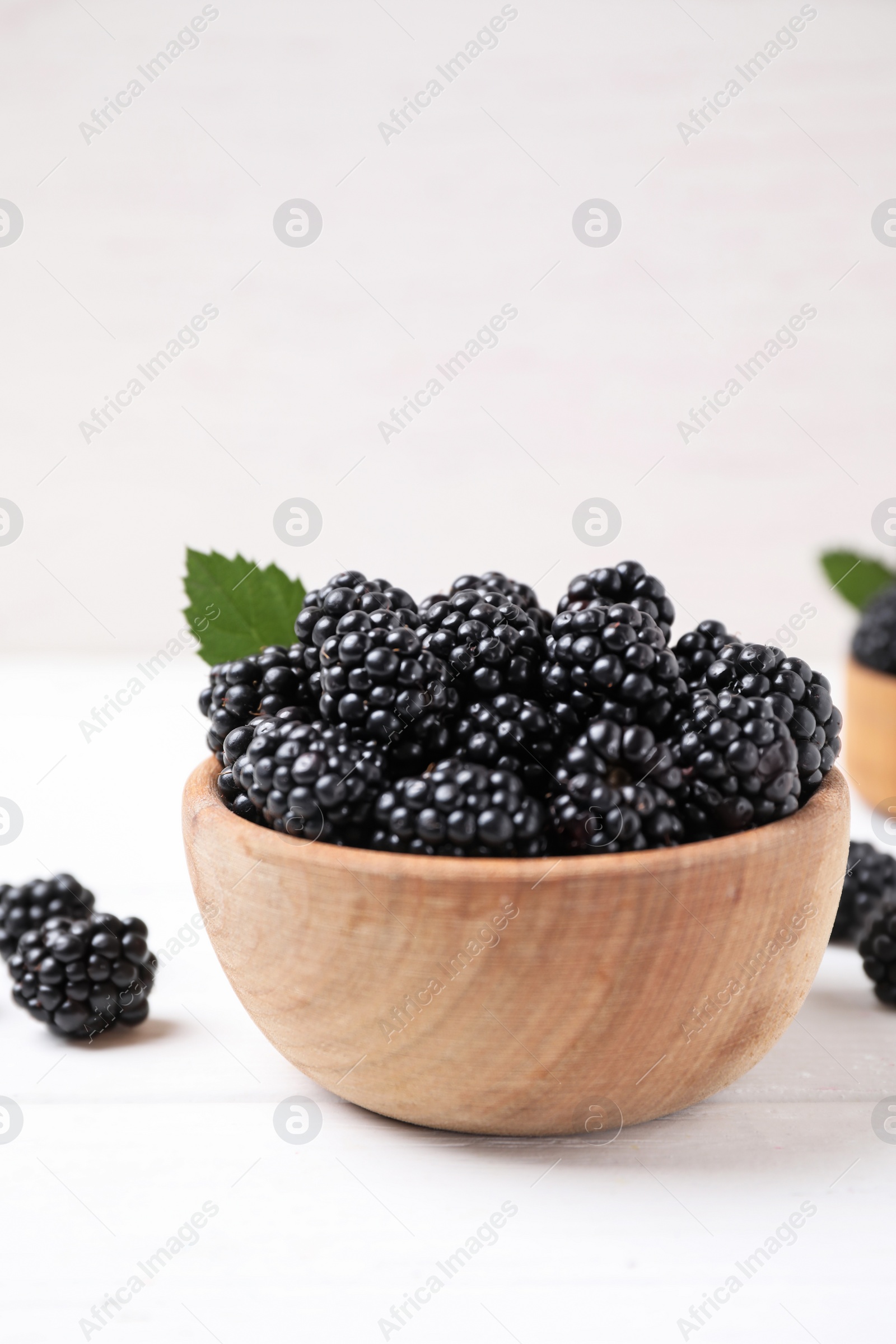 Photo of Fresh ripe blackberries in bowl on white wooden table. Space for text