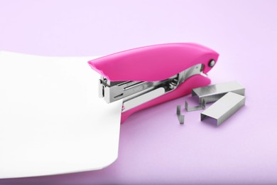 Photo of New bright stapler with paper sheet and staples on violet background