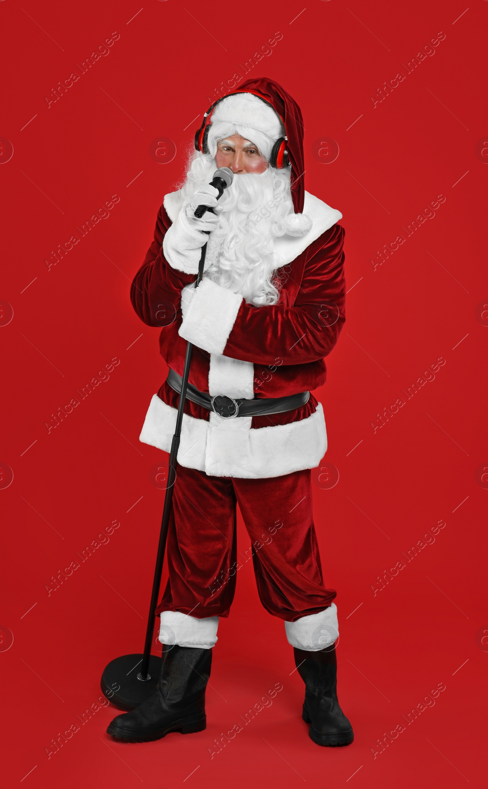 Photo of Santa Claus with headphones and microphone on red background. Christmas music