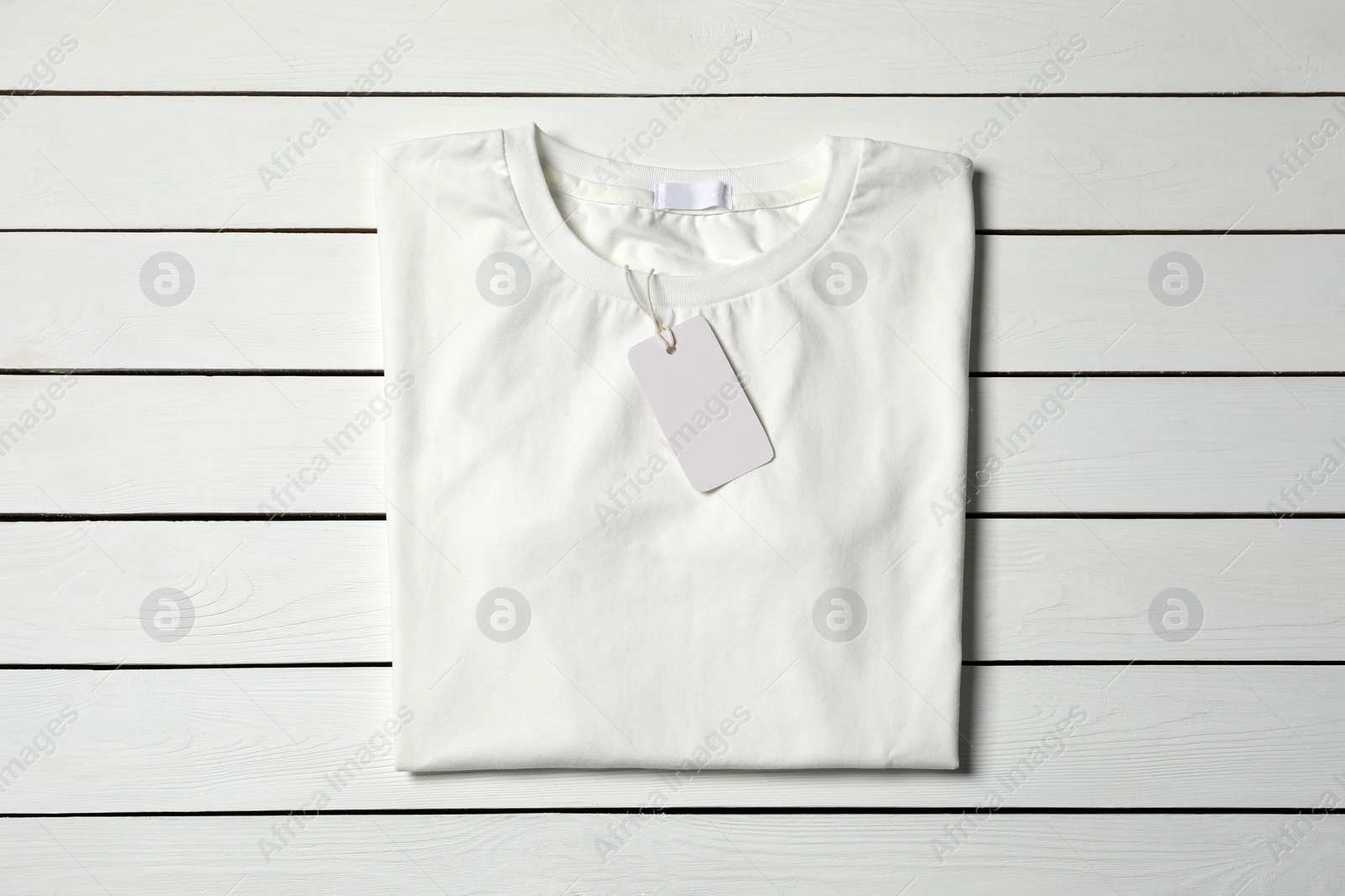 Photo of Stylish T-shirt with label on white wooden table, top view
