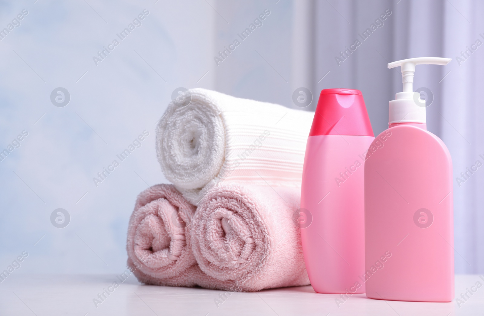 Photo of Bottles of shampoo and rolled bath towels on table, space for text