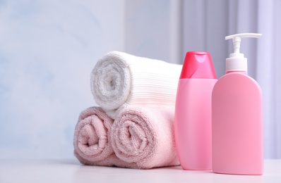 Photo of Bottles of shampoo and rolled bath towels on table, space for text
