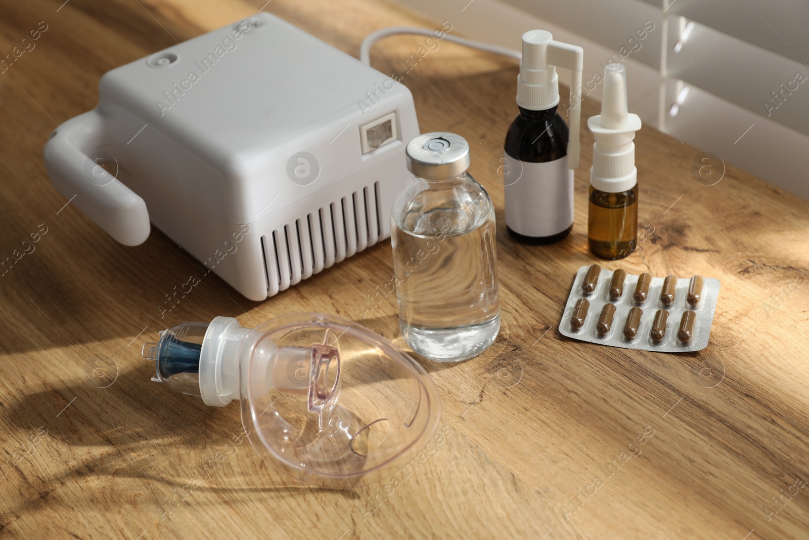 Photo of Modern nebulizer with face mask and medications on wooden table indoors. Inhalation equipment