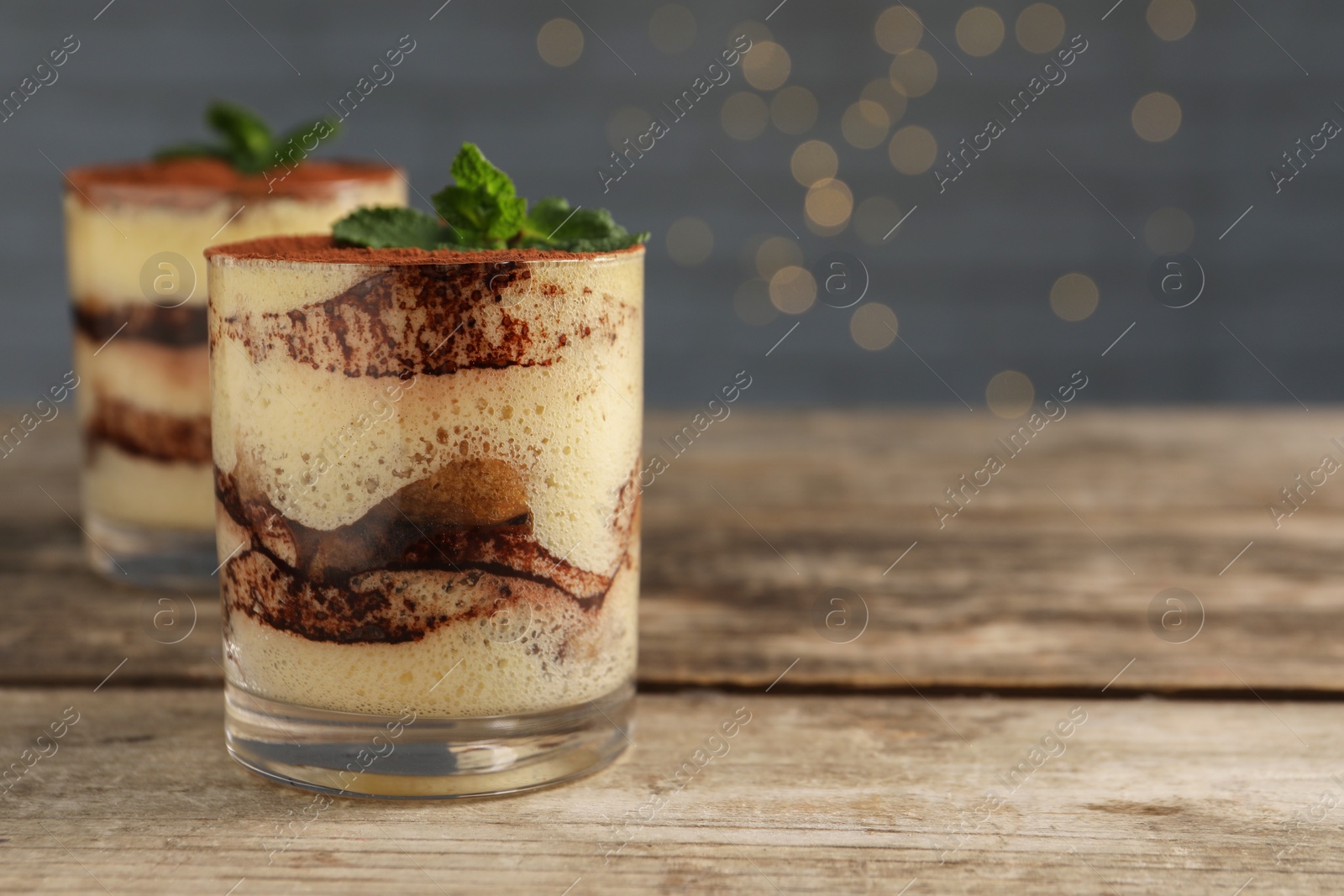 Photo of Tasty tiramisu and mint in glasses on wooden table, closeup. Space for text