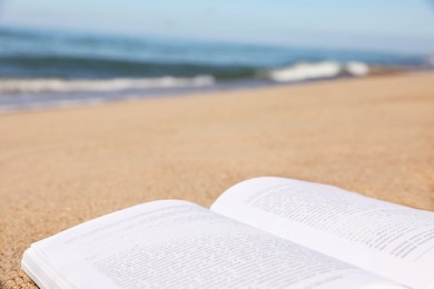 Photo of Open book on sandy beach near sea, closeup. Space for text