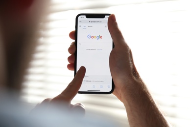 Photo of MYKOLAIV, UKRAINE - OCTOBER 27, 2020: Man using Google search engine on smartphone against blurred background, closeup
