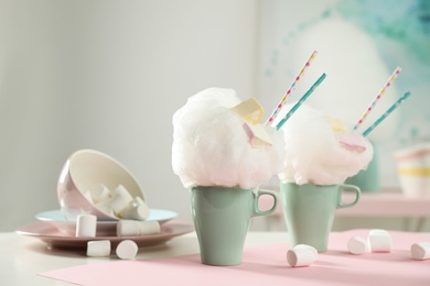 Cups of tasty cotton candy dessert and marshmallow on table, space for text