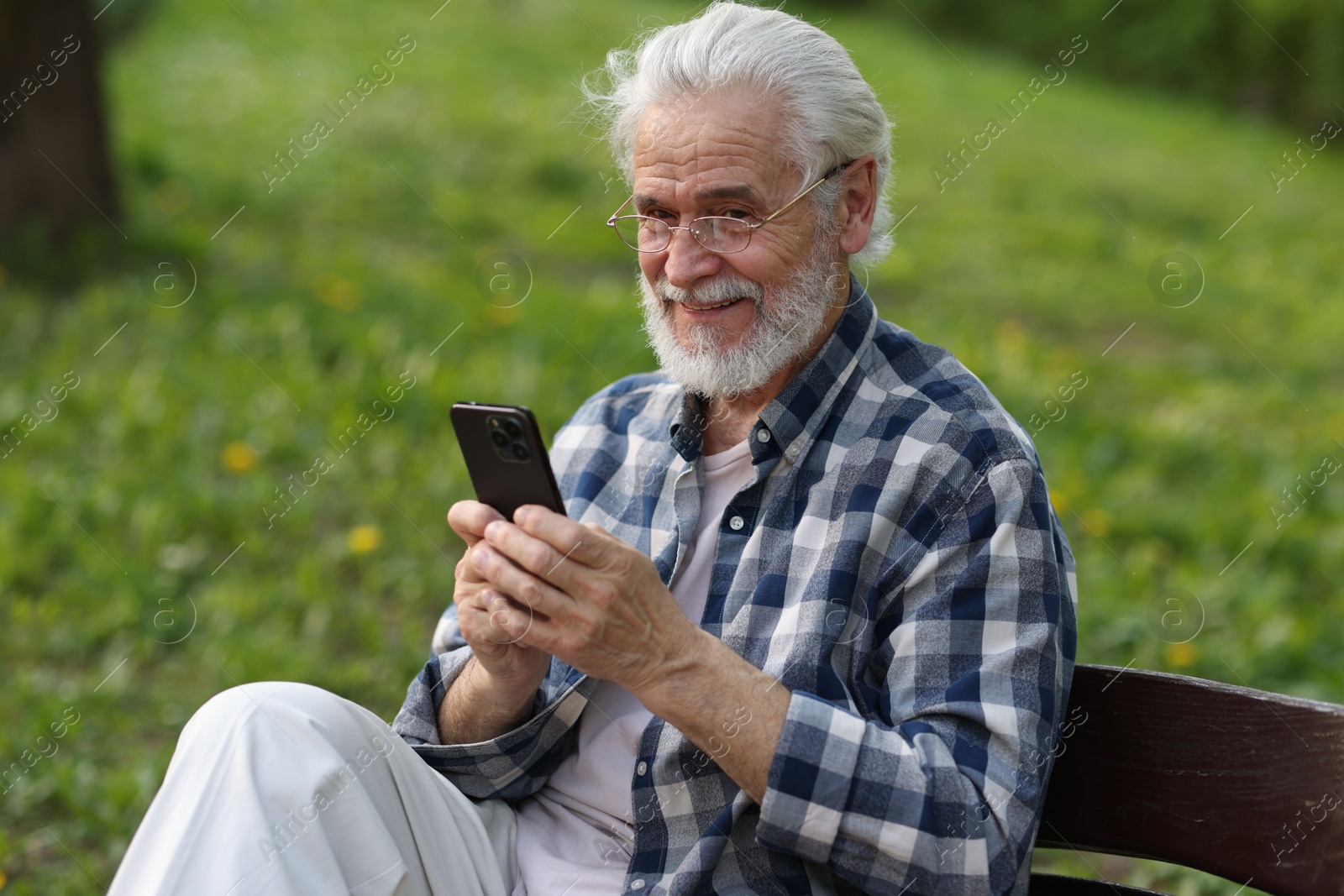 Photo of Portrait of happy grandpa with glasses using smartphone on bench in park