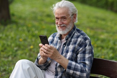 Photo of Portrait of happy grandpa with glasses using smartphone on bench in park