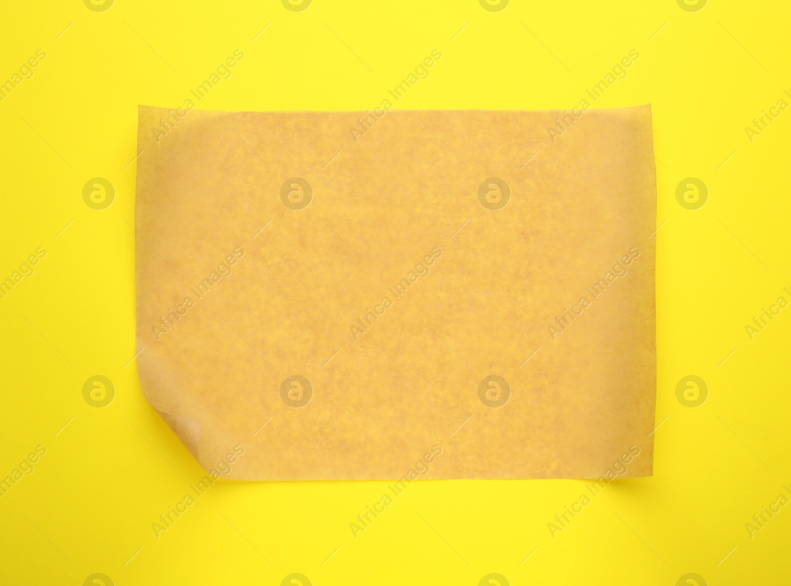 Photo of Sheet of brown baking paper on yellow background, top view