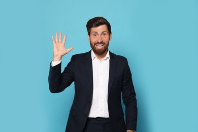 Smiling bearded man in suit showing hand on light blue background