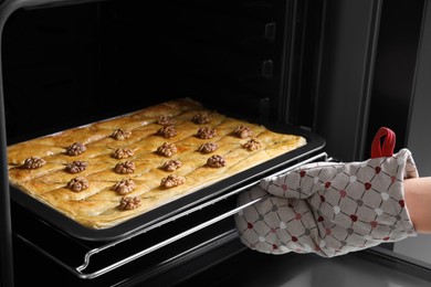 Photo of Woman taking out baking pan with delicious baklava from oven, closeup