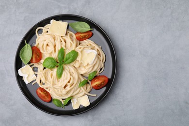 Delicious pasta with brie cheese, tomatoes and basil leaves on grey table, top view. Space for text