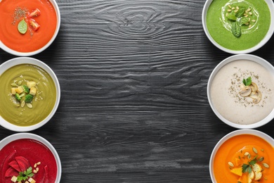 Various soups in bowls and space for text on wooden background, top view. Healthy food