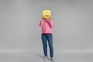 Photo of Woman holding emoticon with stars instead of eyes on grey background