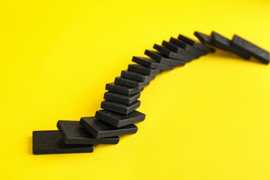Photo of Falling black domino tiles on yellow background