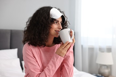 Photo of Beautiful young woman in stylish pyjama and sleep mask with cup of drink at home