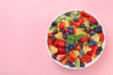 Yummy fruit salad in bowl on pink background, top view. Space for text