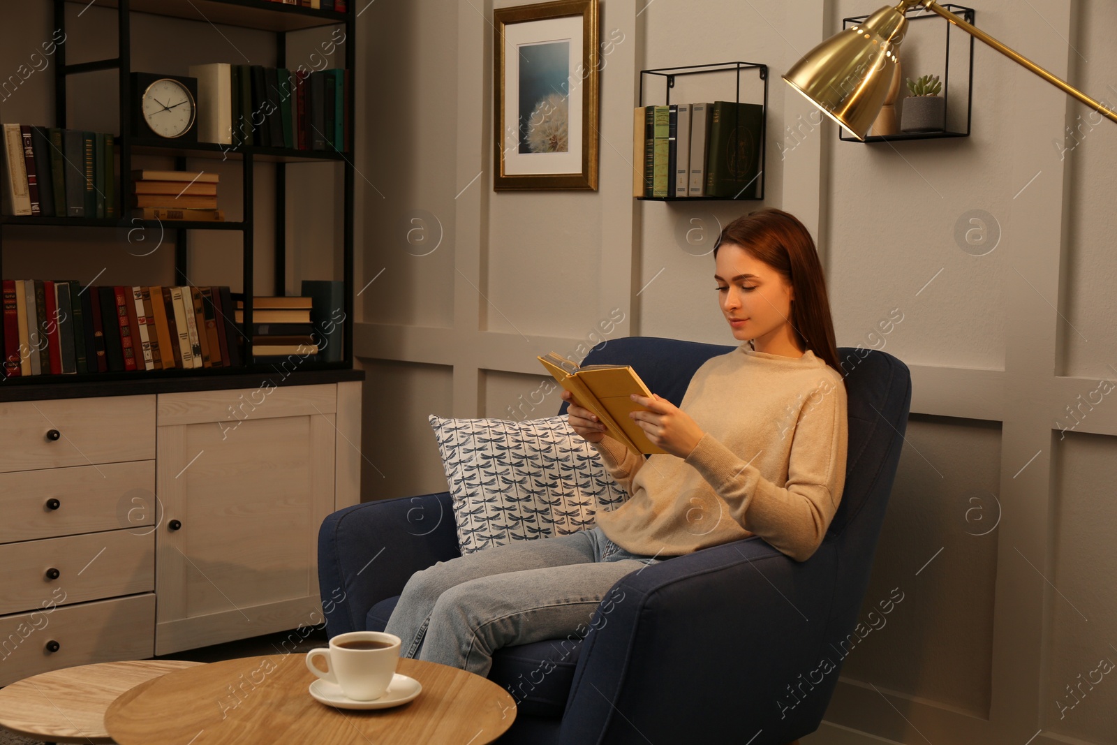 Photo of Young woman reading book in armchair indoors. Home library