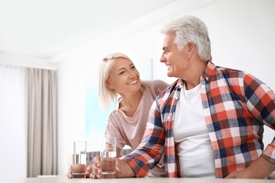 Photo of Affectionate senior couple with glasses of water at home. Space for text