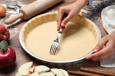Photo of Woman making holes in raw dough with fork at wooden table, closeup. Baking apple pie