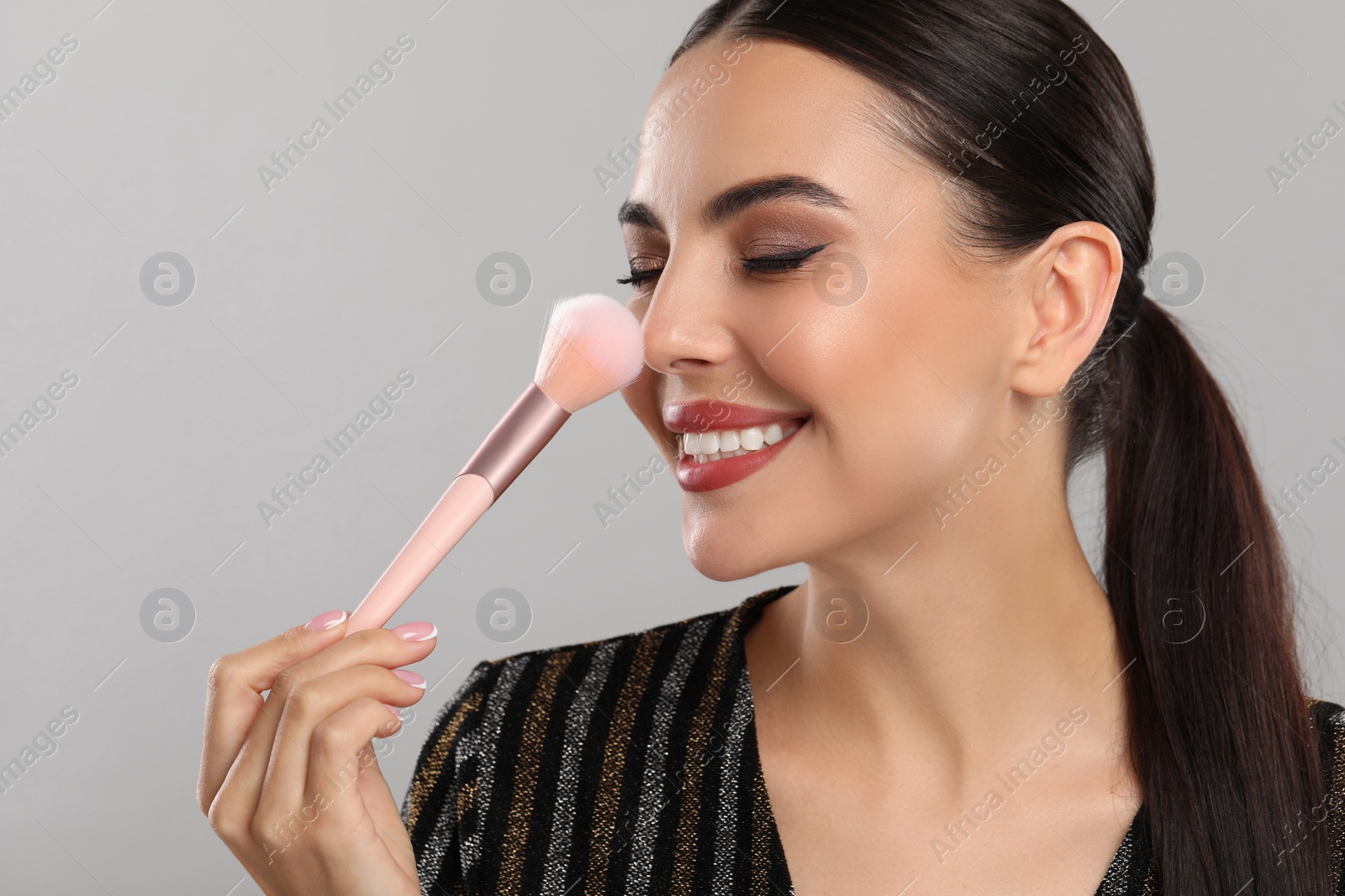 Photo of Everyday makeup. Beautiful woman applying face powder on light grey background, space for text