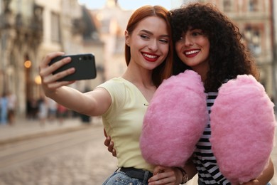 Photo of Happy friends with pink cotton candies taking selfie on city street