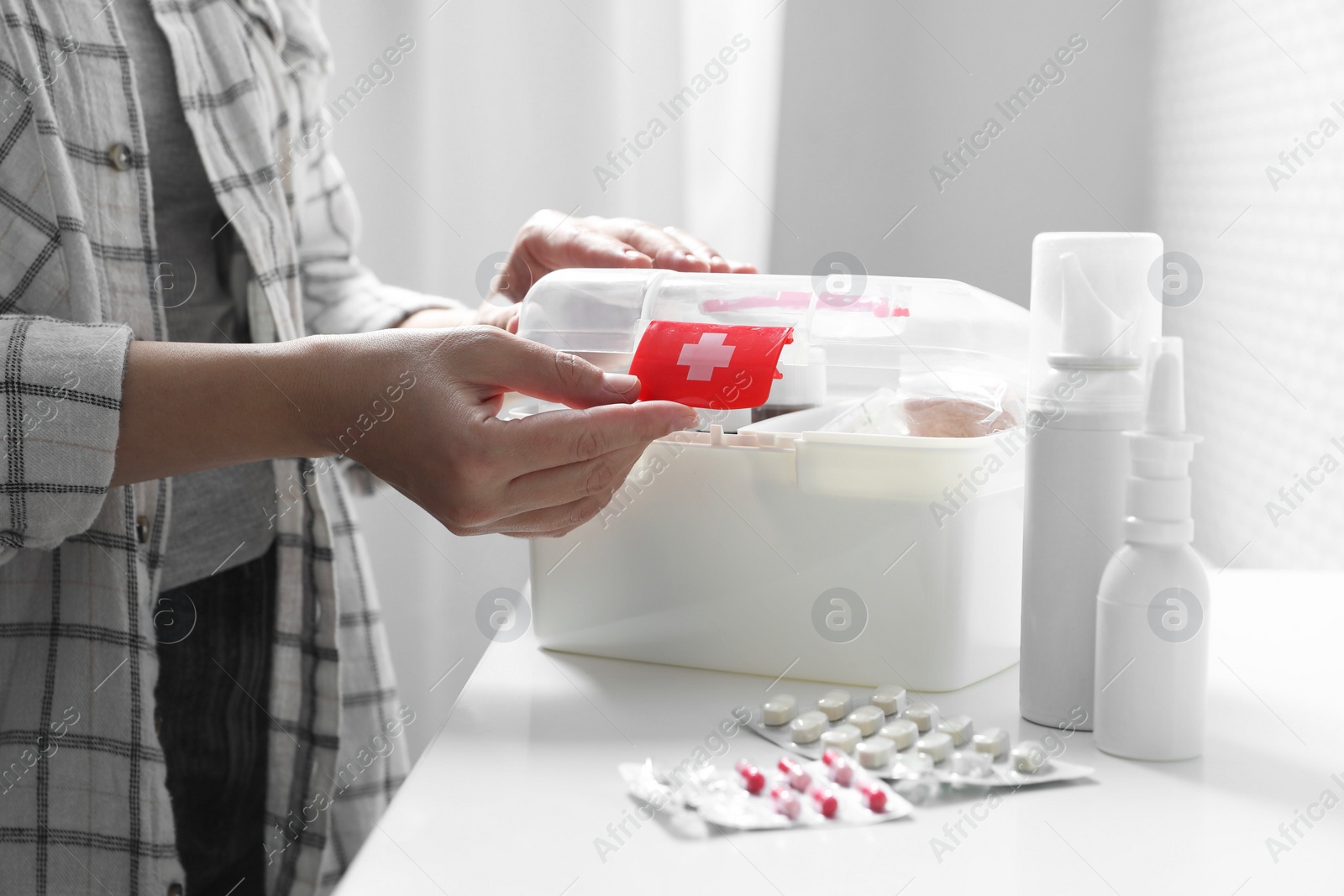 Photo of Woman opening first aid kit at white table indoors, closeup