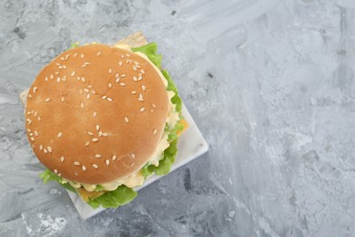 Photo of Delicious cheeseburger on grey textured table, top view. Space for text
