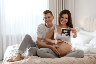 Photo of Young pregnant woman and her husband with ultrasound picture of baby in bedroom