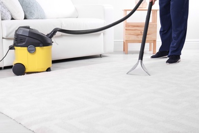 Man cleaning carpet with vacuum cleaner, closeup. Space for text