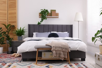 Stylish bedroom with double bed and beautiful green houseplants. Modern interior