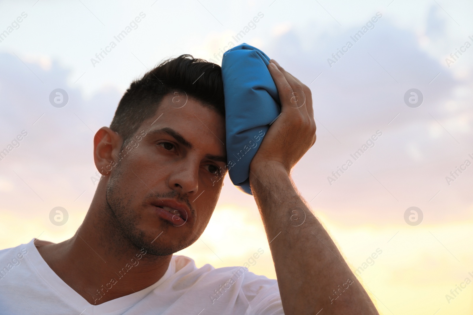 Photo of Man with cold pack suffering from heat stroke outdoors at sunset