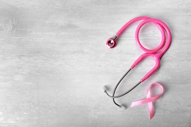 Pink ribbon and stethoscope on light background, top view with space for text. Breast cancer concept