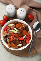 Photo of Delicious beef stew with carrots, chili peppers, green onions and potatoes served on white textured table, flat lay