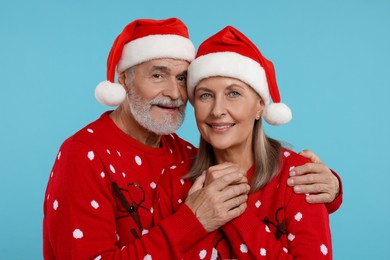 Photo of Senior couple in Christmas sweaters and Santa hats on light blue background