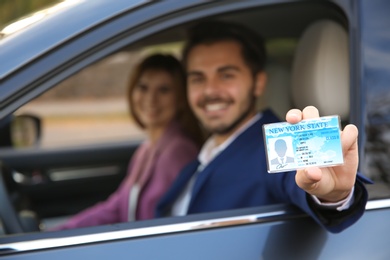 Photo of Young man holding driving license in car with passenger. Space for text